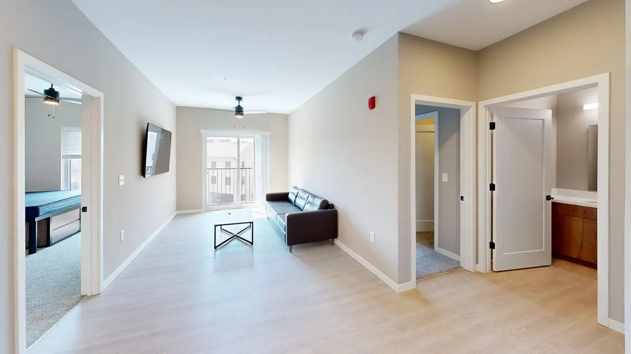 Bright and modern open-concept living room with natural light, sleek flooring, and a cozy seating area, adjacent to a bedroom and bathroom.