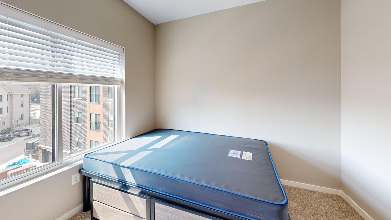 Bright bedroom with a large window, new mattress, neutral tones, and urban view.