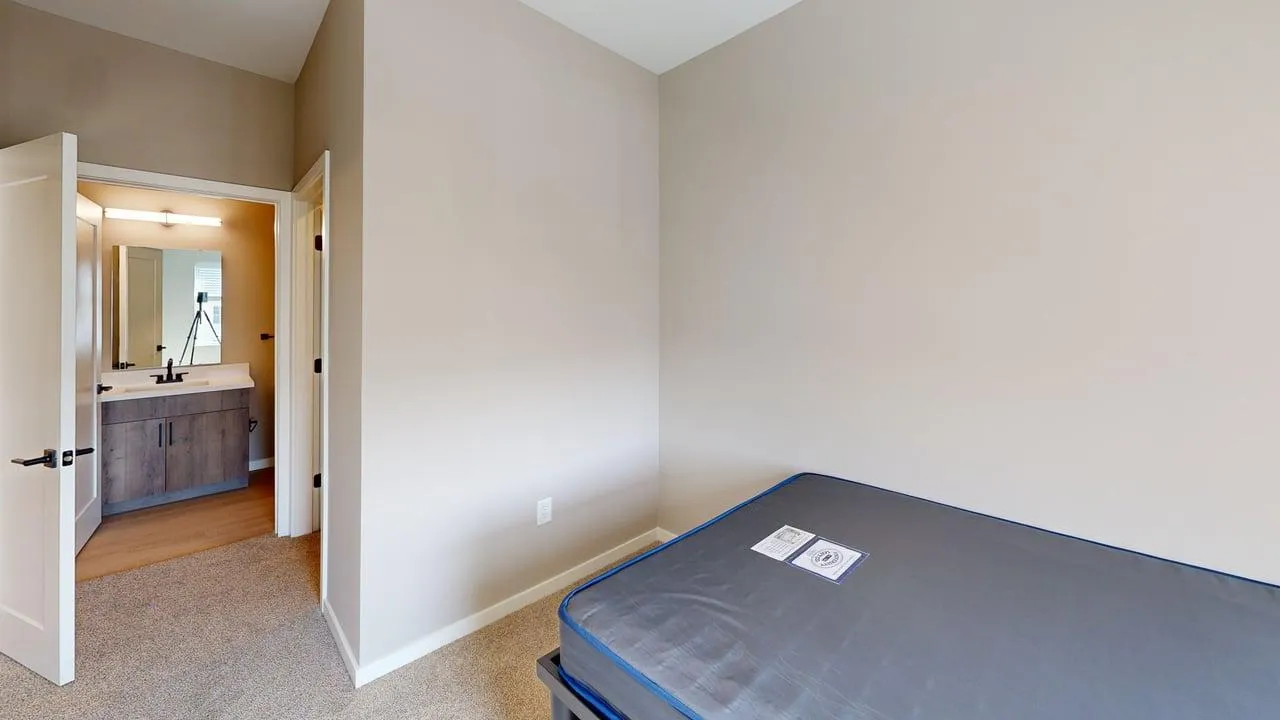 Cozy bedroom with plush carpet, featuring a neatly made bed and an adjoining modern bathroom with a stylish vanity.