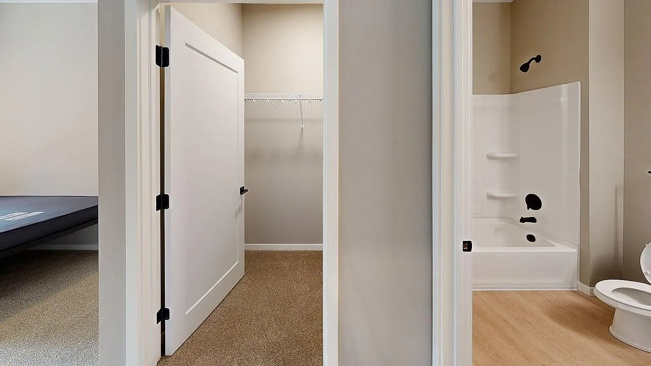 Inviting interior showcasing a minimalist walk-in closet, pristine bathroom with modern fixtures, and entry to a cozy bedroom.