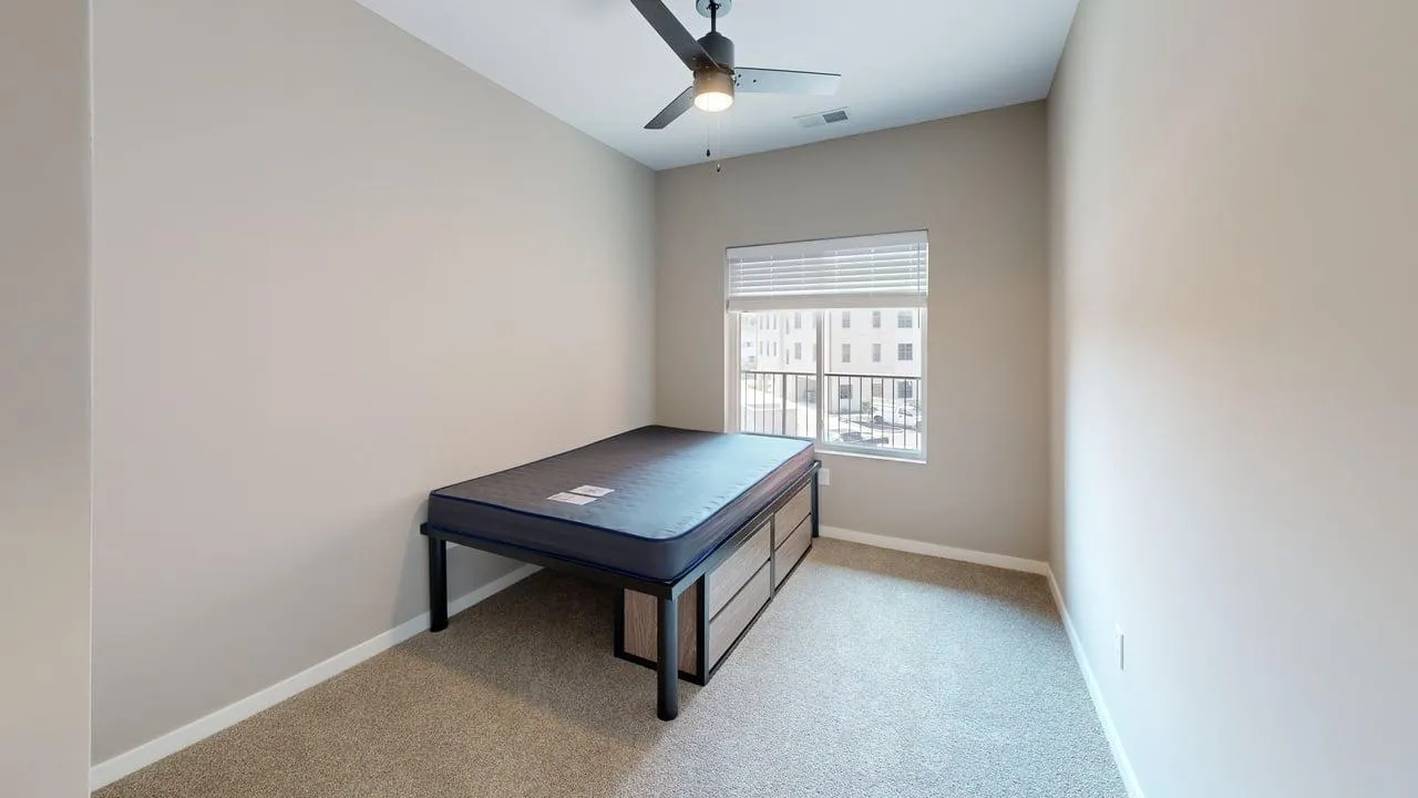 Bright and cozy bedroom with a modern ceiling fan, large window offering natural light, and a stylish twin bed frame.