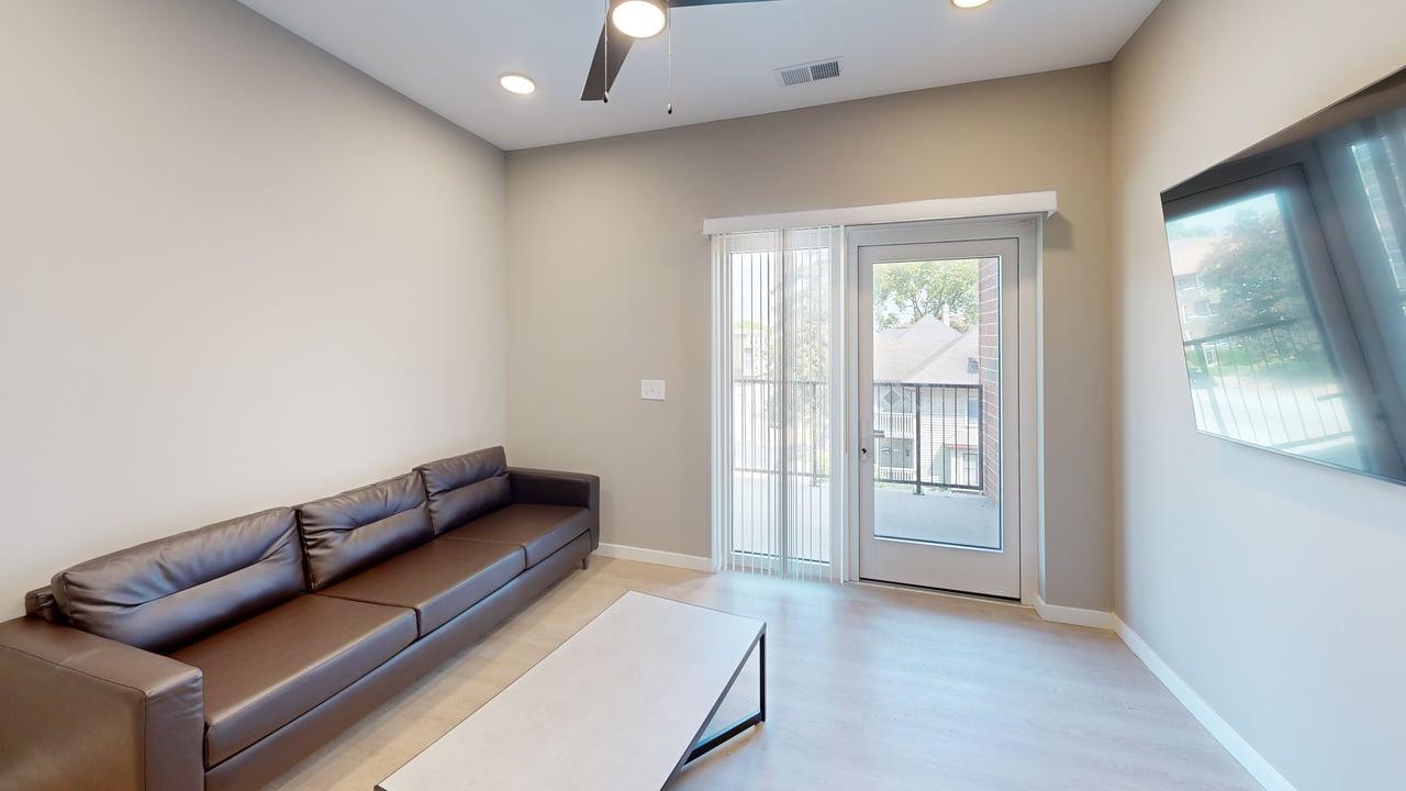 Modern living room featuring a sleek brown leather sofa, large windows with natural light, and a cozy balcony view.