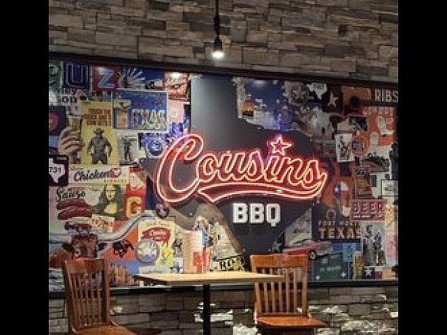 Vibrant interior wall showcasing a neon 'Cousins BBQ' sign surrounded by eclectic vintage posters, capturing a rustic and lively atmosphere.