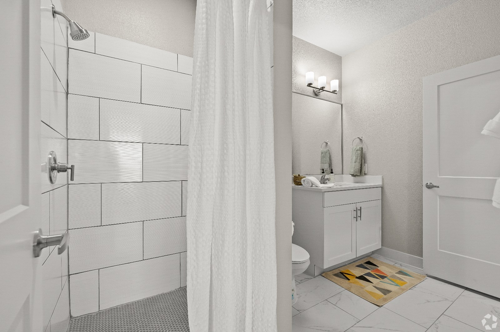 Modern bathroom with elegant white tile shower, cozy vanity area, and stylish lighting fixtures.