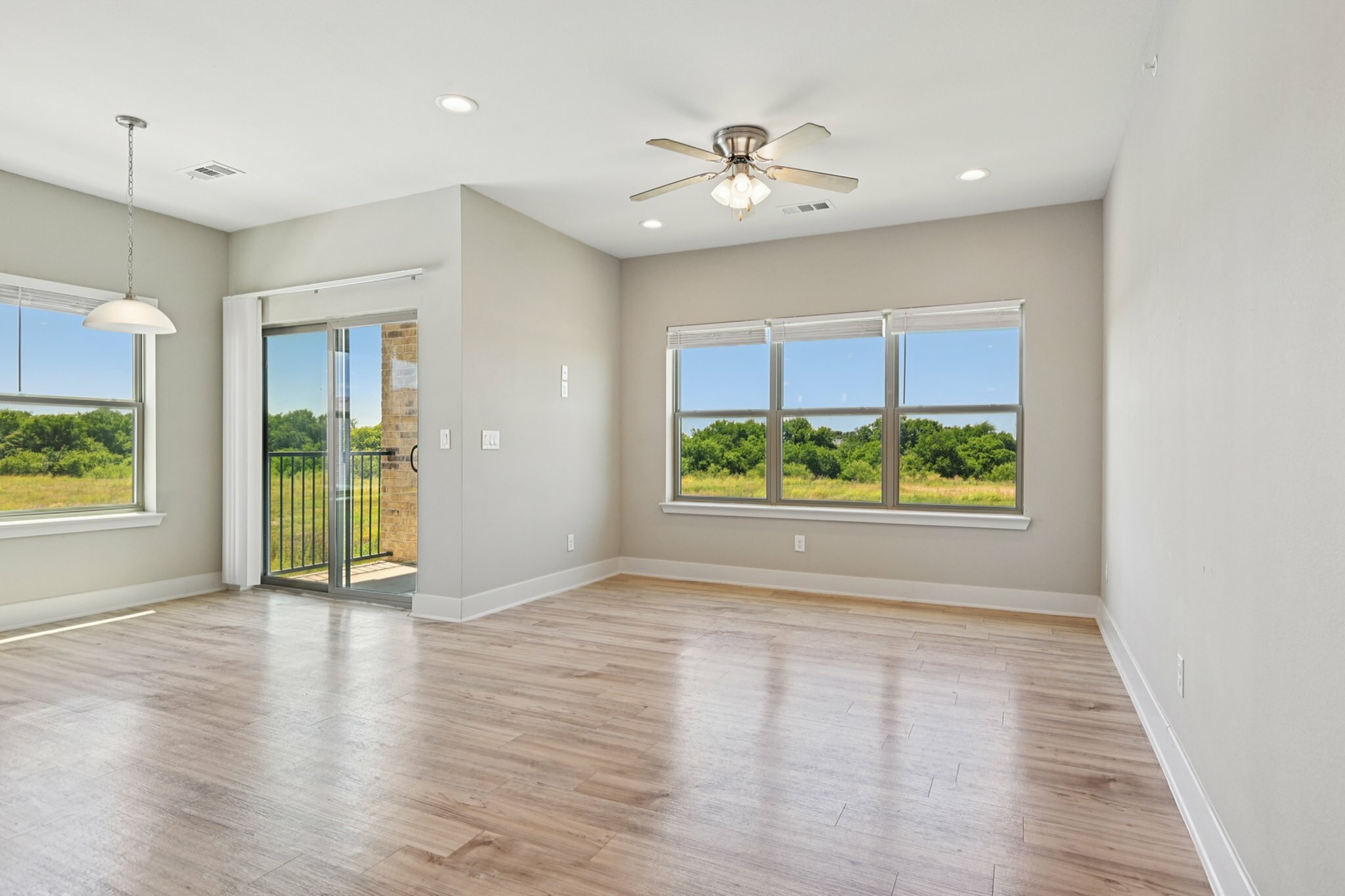 Bright and airy living space with wood flooring and scenic views, featuring large windows and a ceiling fan, perfect for a tranquil home setting.
