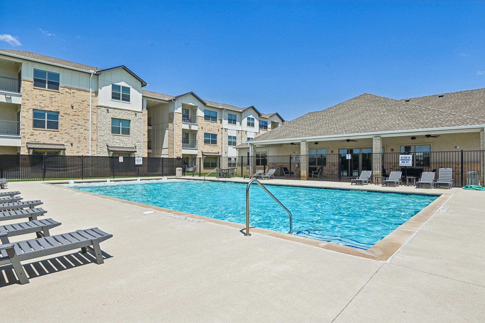Inviting apartment complex featuring a sparkling outdoor pool and sunlit lounge area, perfect for relaxation and enjoyment.