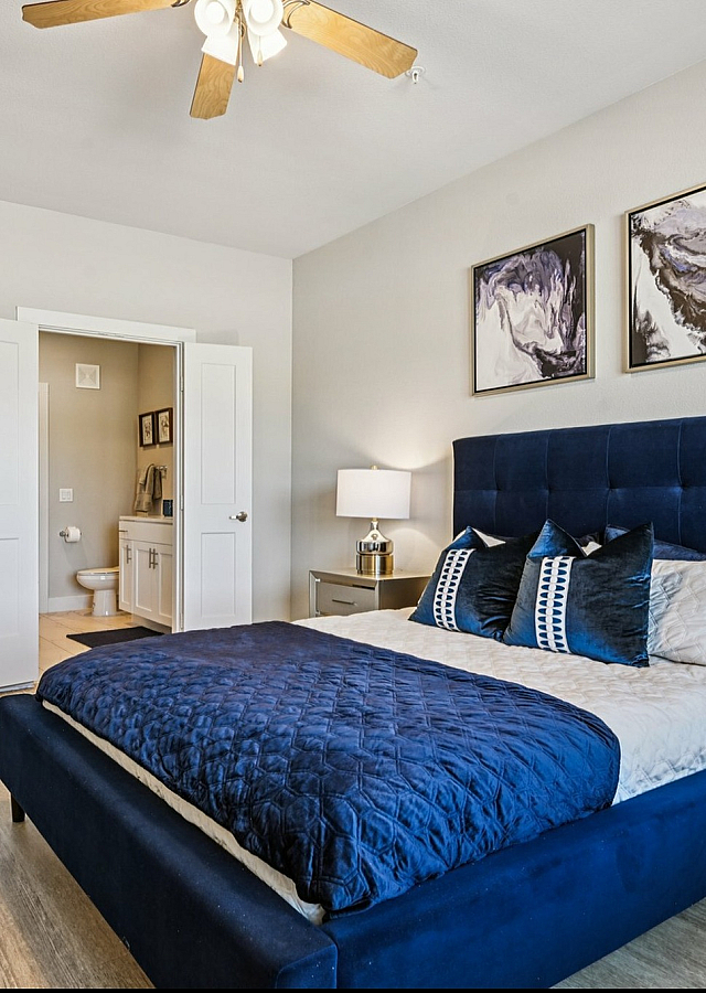 Luxurious bedroom with elegant blue bed, stylish artwork, and en-suite bathroom in upscale apartment.