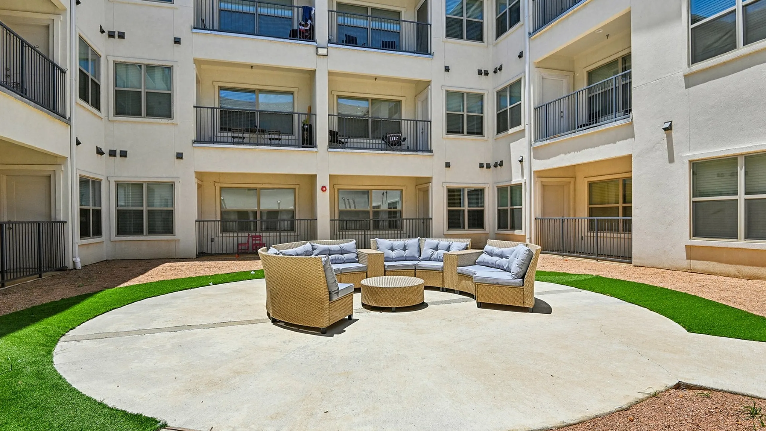 Inviting apartment courtyard featuring a circular seating arrangement, surrounded by a modern three-story building with private balconies.