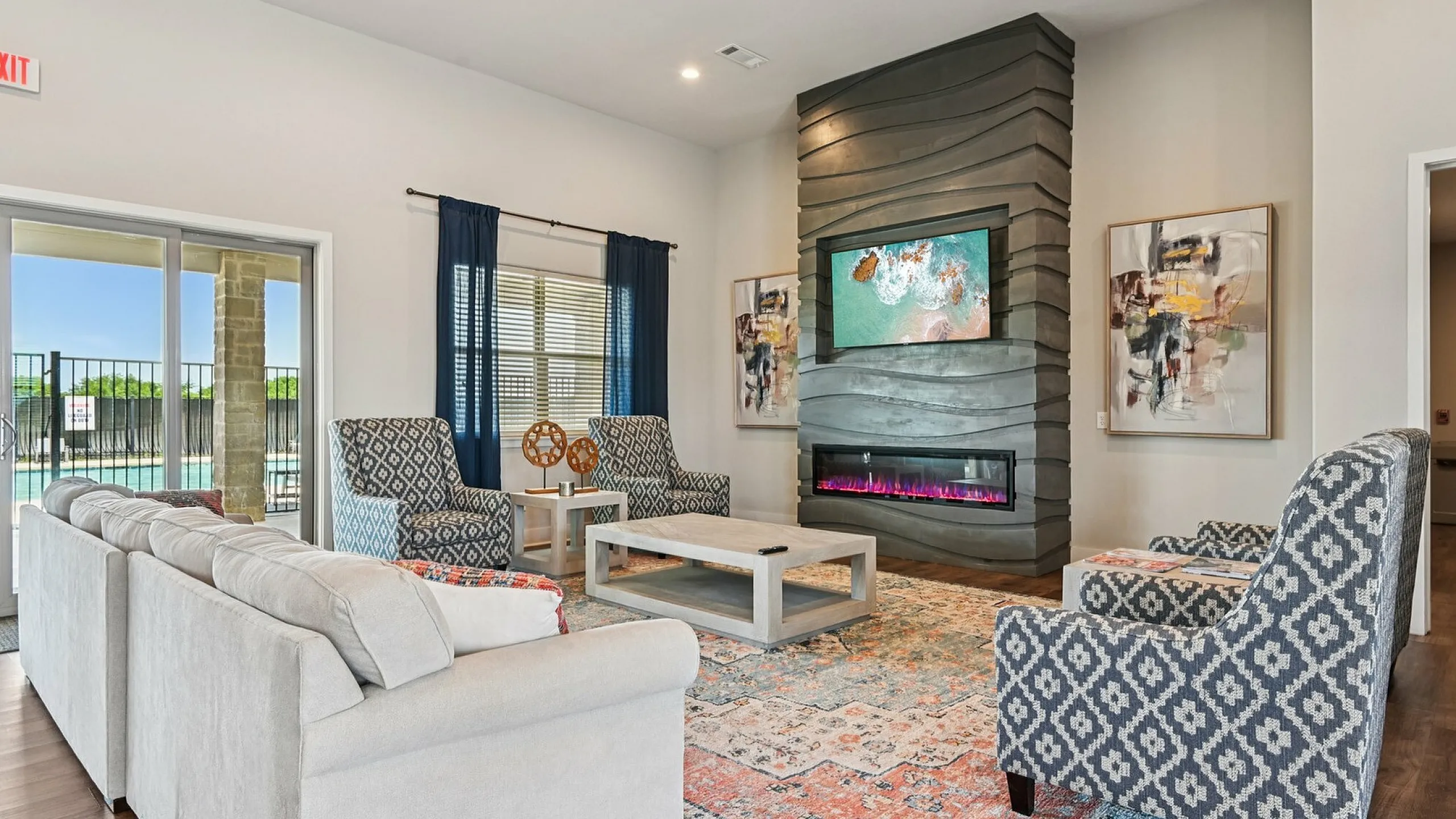 Elegant living room featuring a modern fireplace, chic patterned chairs, and plush sofas, complemented by large windows and vibrant artwork.
