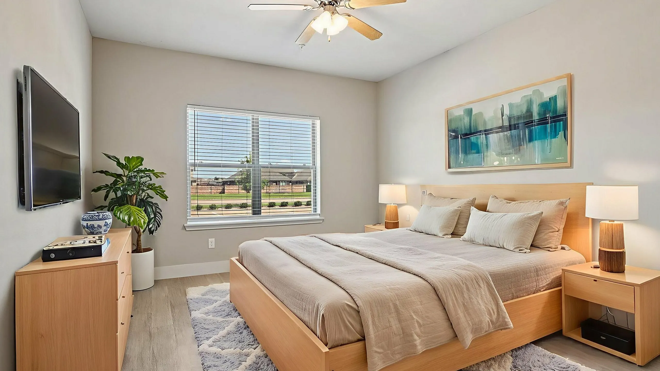 Inviting bedroom with modern decor, featuring a cozy bed, elegant lamps, and a serene artwork on the wall. The room is brightened by natural light from a large window overlooking a peaceful outdoor view.