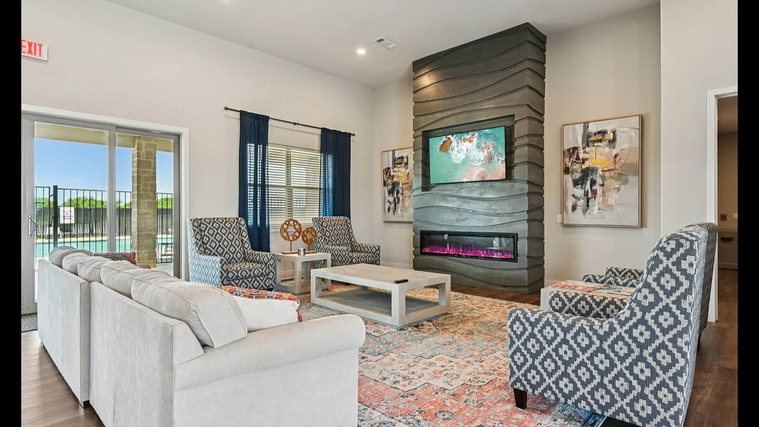 Inviting living room with stylish patterned chairs, a plush sectional sofa, modern fireplace, and abstract artwork, offering a cozy ambiance and pool view through large sliding glass doors.