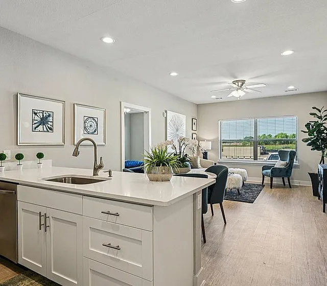 Chic open-concept living space featuring a modern kitchen with white cabinetry and a bright, inviting living room with large windows and tasteful decor.