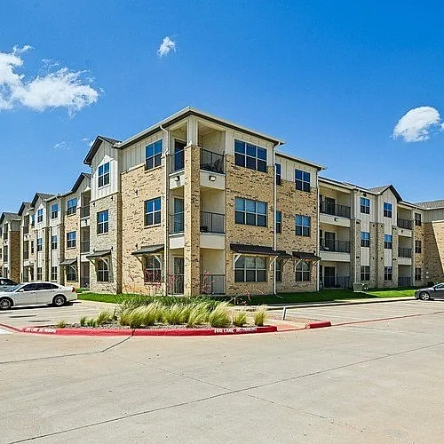 Charming modern apartment complex with spacious parking and attractive architecture beneath a bright blue sky.