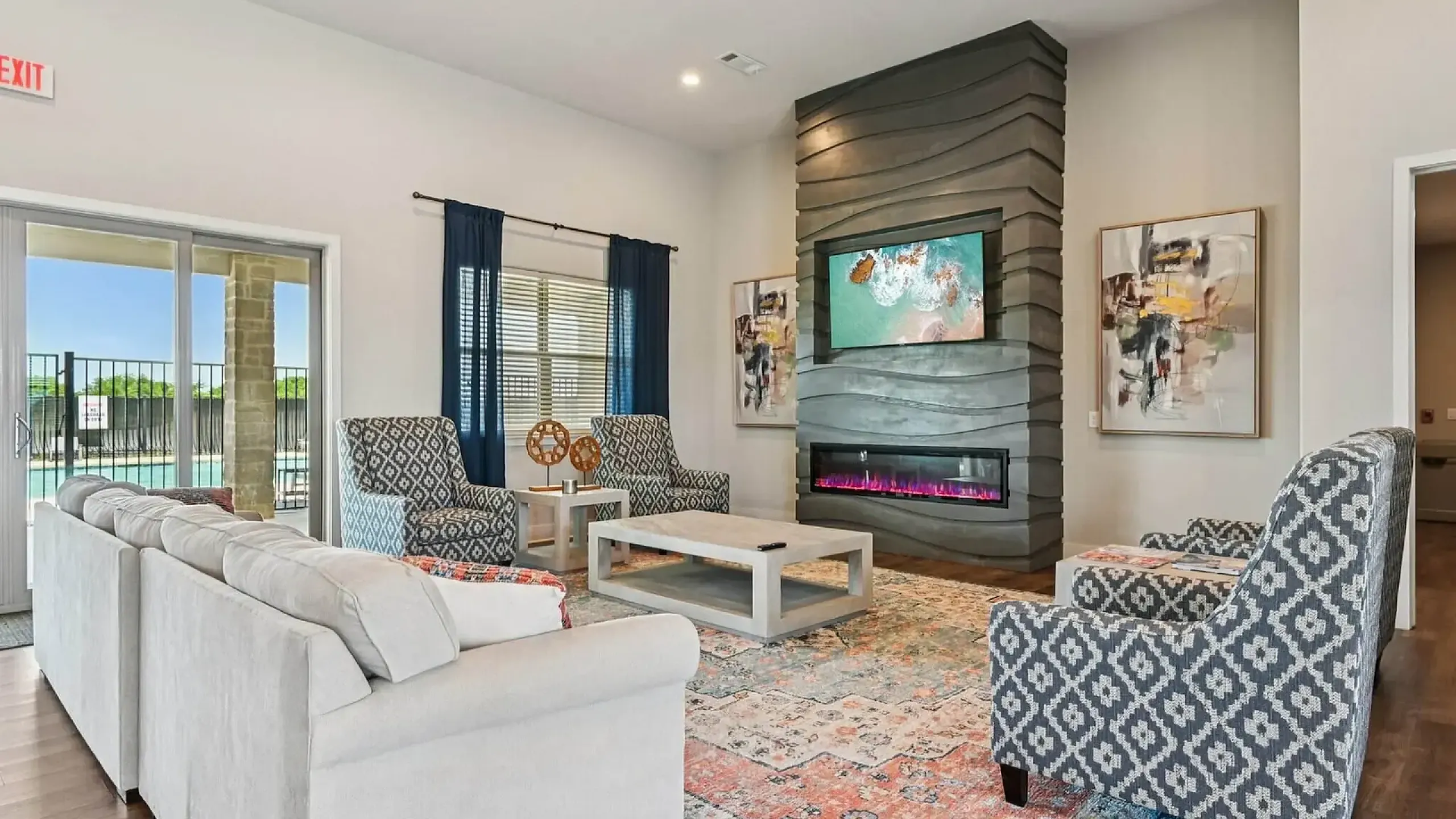 Inviting living room with stylish patterned chairs, a plush sectional sofa, modern fireplace, and abstract artwork, offering a cozy ambiance and pool view through large sliding glass doors.
