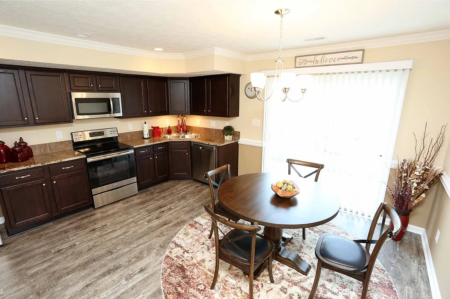 Inviting kitchen and dining area with rich dark cabinetry, modern appliances, and elegant chandelier lighting over a cozy round table.