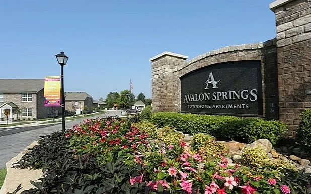 Welcoming entrance to Avalon Springs Townhome Apartments with lush landscaping and elegant signage.