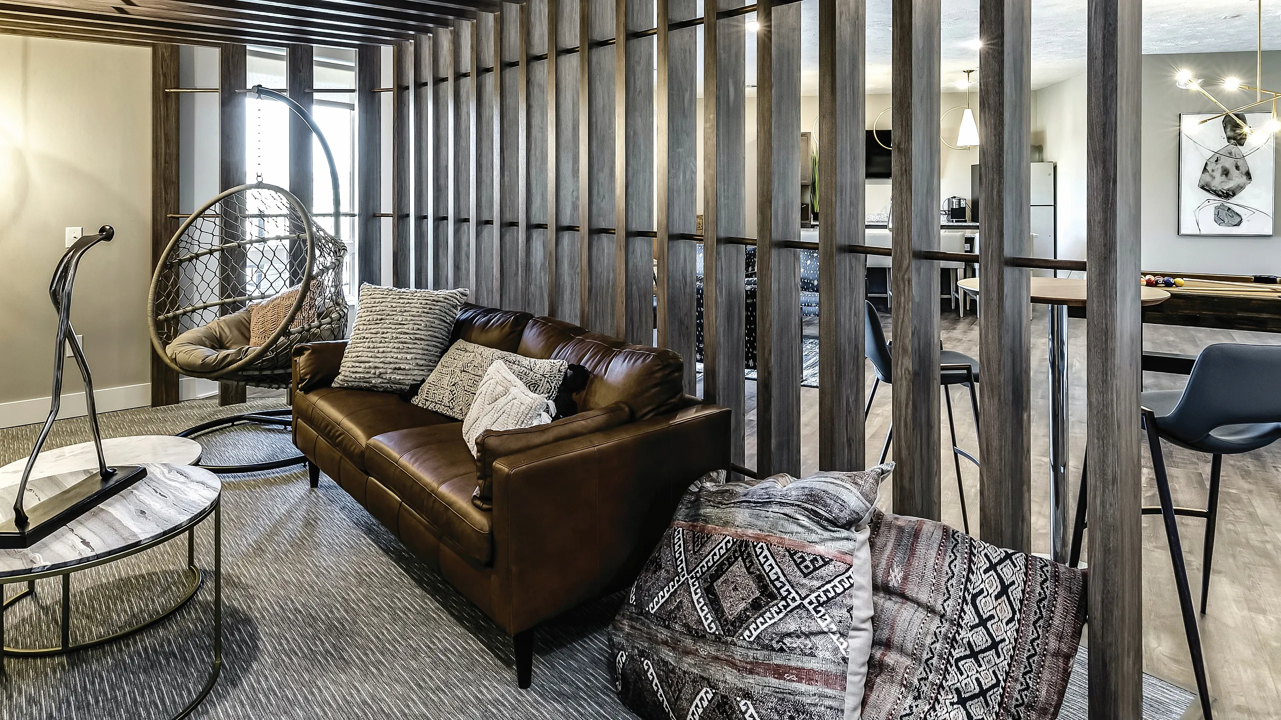 Chic apartment lounge with a cozy leather sofa and stylish hanging chair, complemented by modern wood paneling and elegant decor.