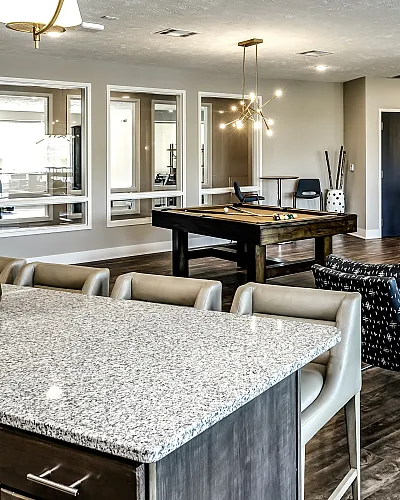 Luxurious apartment lounge featuring a modern kitchen island, stylish seating, and an elegant pool table in a spacious, well-lit setting.