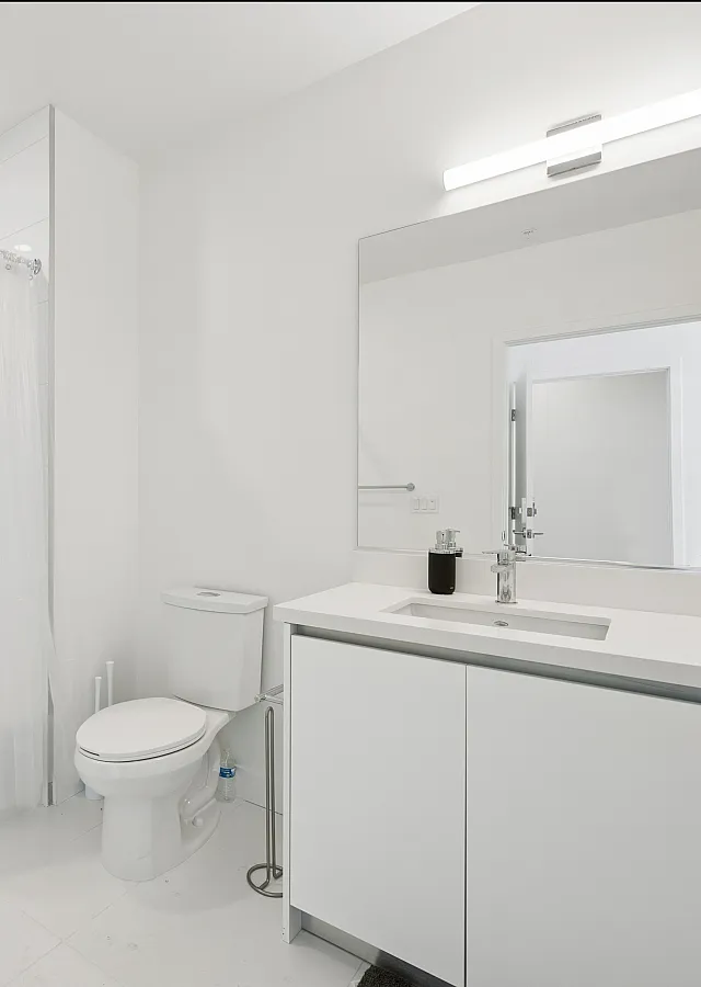 Sleek modern bathroom featuring a pristine white bathtub, elegant vanity with ample storage, and a large illuminated mirror ideal for a refreshing start to the day.