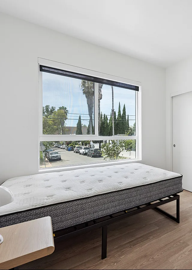 Bright and airy bedroom with sleek flooring and large window overlooking a scenic street view.