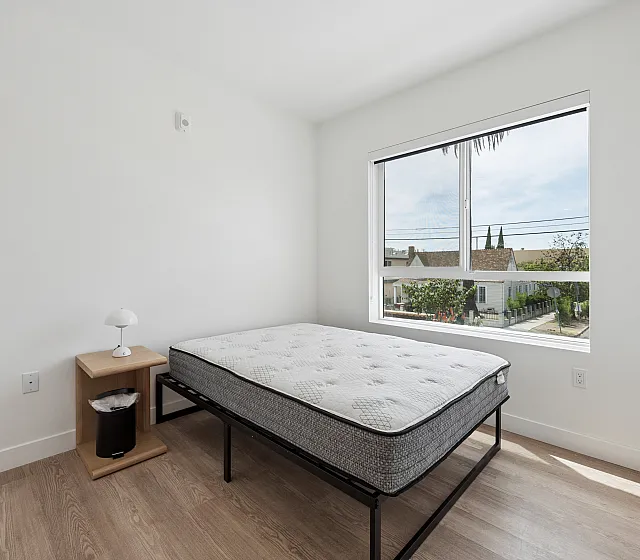 Bright and modern bedroom with large window, comfortable bed, and minimalist decor, offering a serene and inviting atmosphere.