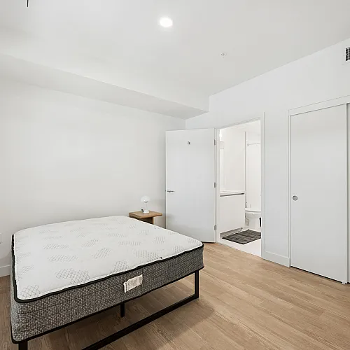 Bright modern bedroom with sleek hardwood floors, a cozy bed, and convenient ensuite bathroom for luxurious living.