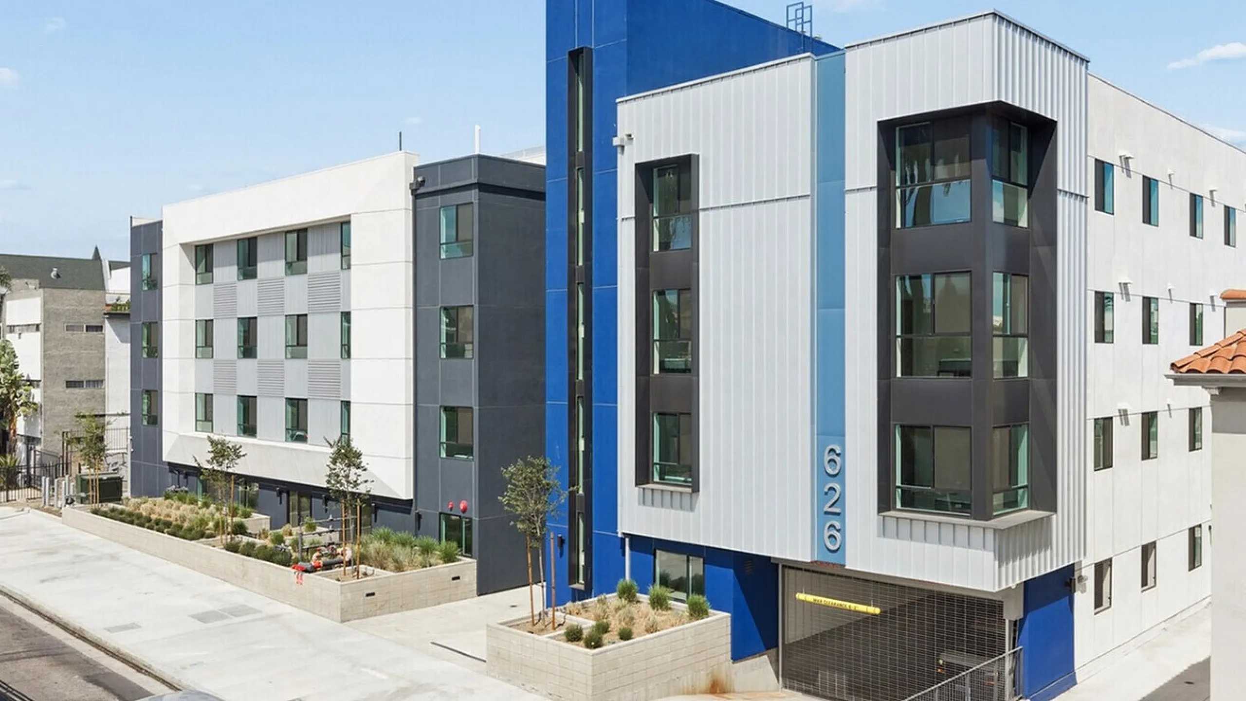 Modern apartment building with sleek architectural design featuring large windows, vibrant blue accents, and a landscaped entrance.