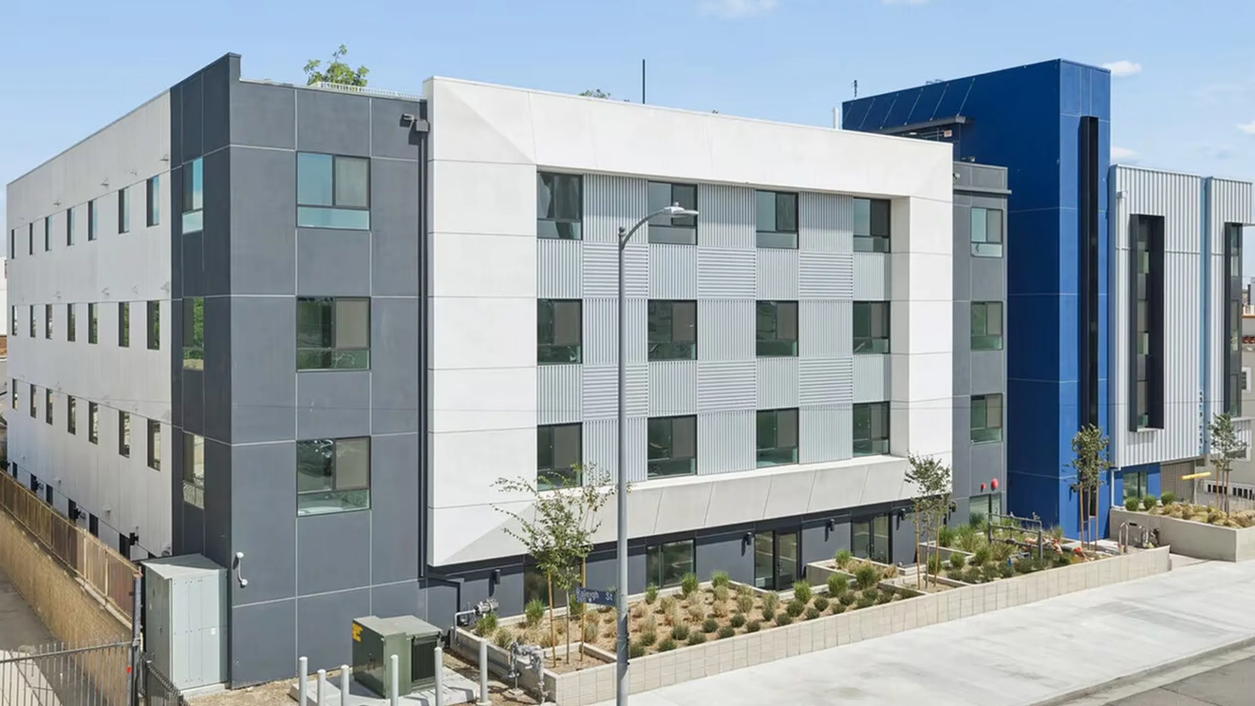 Modern apartment complex showcasing sleek architecture with vibrant blue accents, large windows, and landscaped surroundings under a bright sky.
