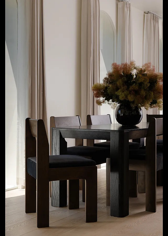 Elegant dining room with modern dark wood furniture and a lush floral arrangement, bathed in natural light from large windows.