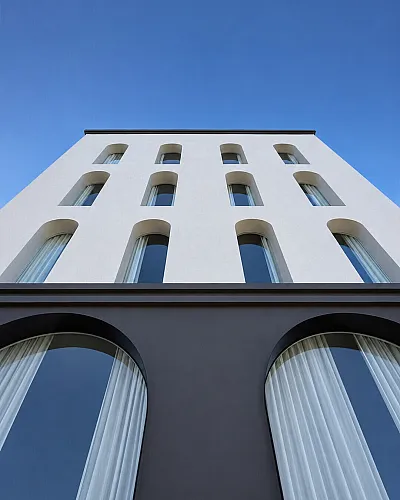 Sleek modern apartment building facade with distinctive arched windows against a clear blue sky.