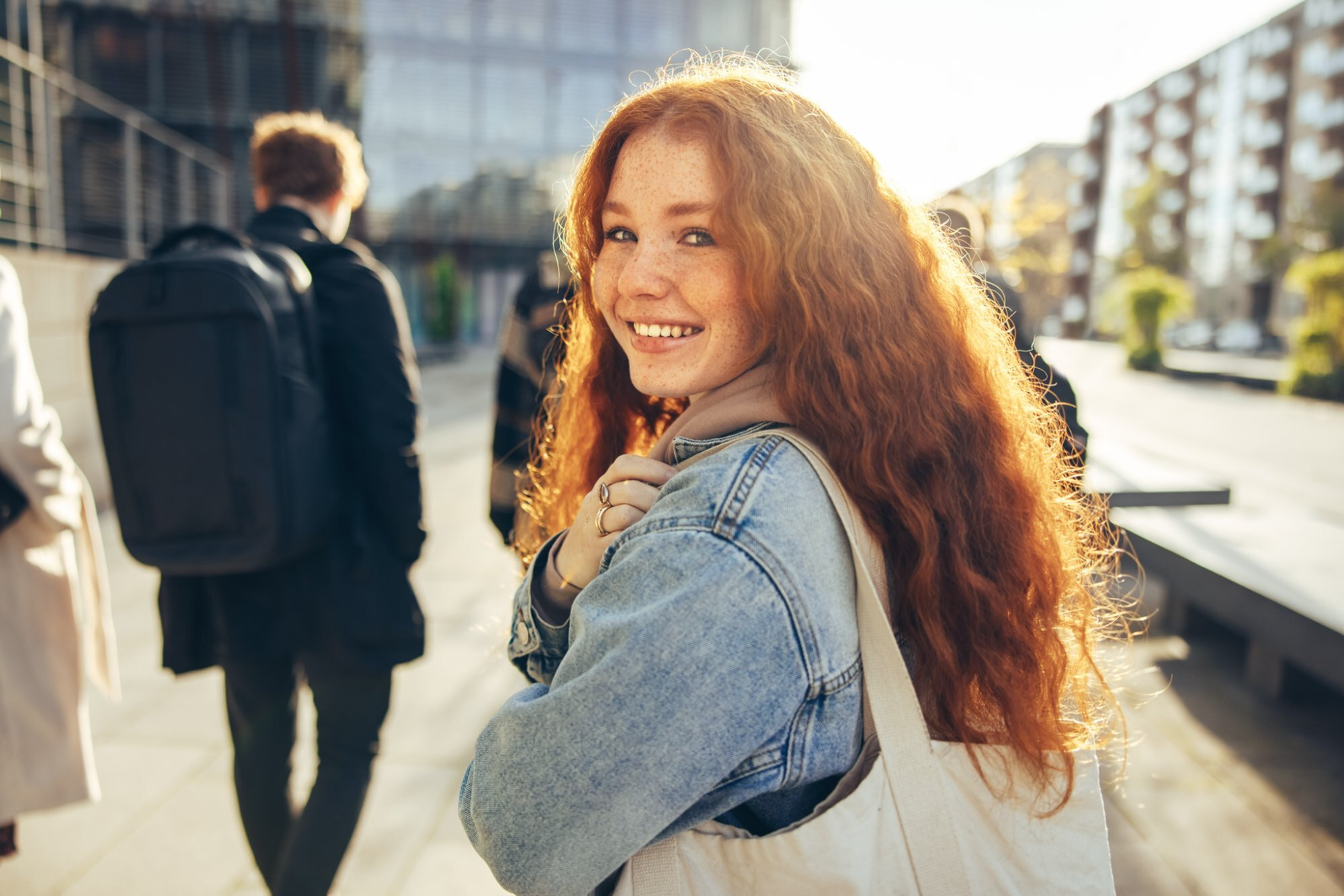 Smiling BYU student with a tote bag walking with friends on a sunny campus sidewalk