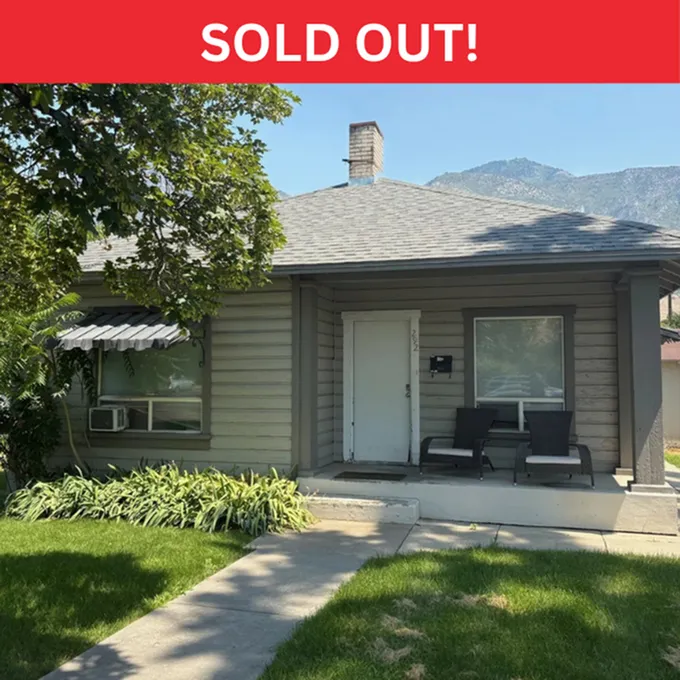 Charming single-story home with cozy front porch, nestled amidst lush greenery and mountain views. Marked as sold out.
