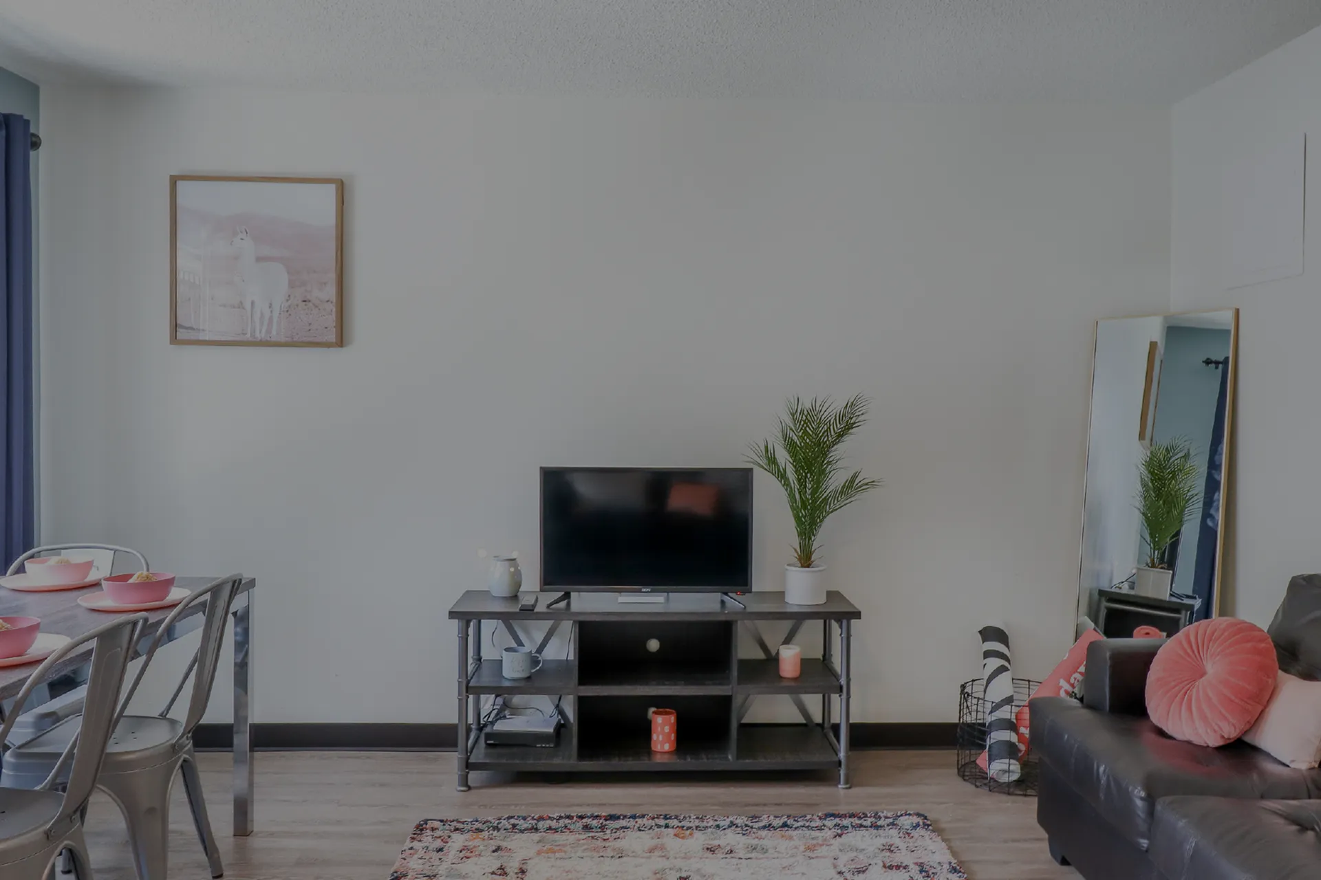 Chic apartment living room with a cozy sofa, elegant wooden TV stand, and a modern dining set. A stylish floor lamp and vibrant decor enhance the inviting ambiance.