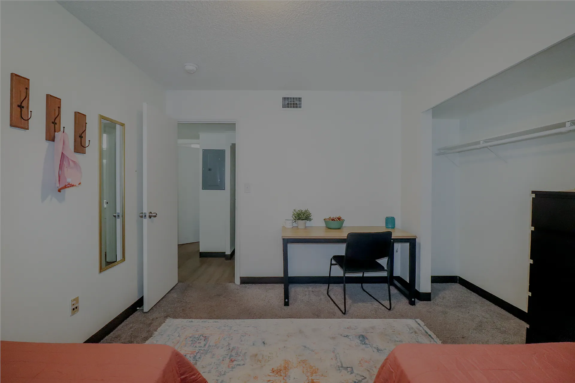 Cozy bedroom featuring a minimalist desk setup, built-in closet, and warm carpeted flooring.