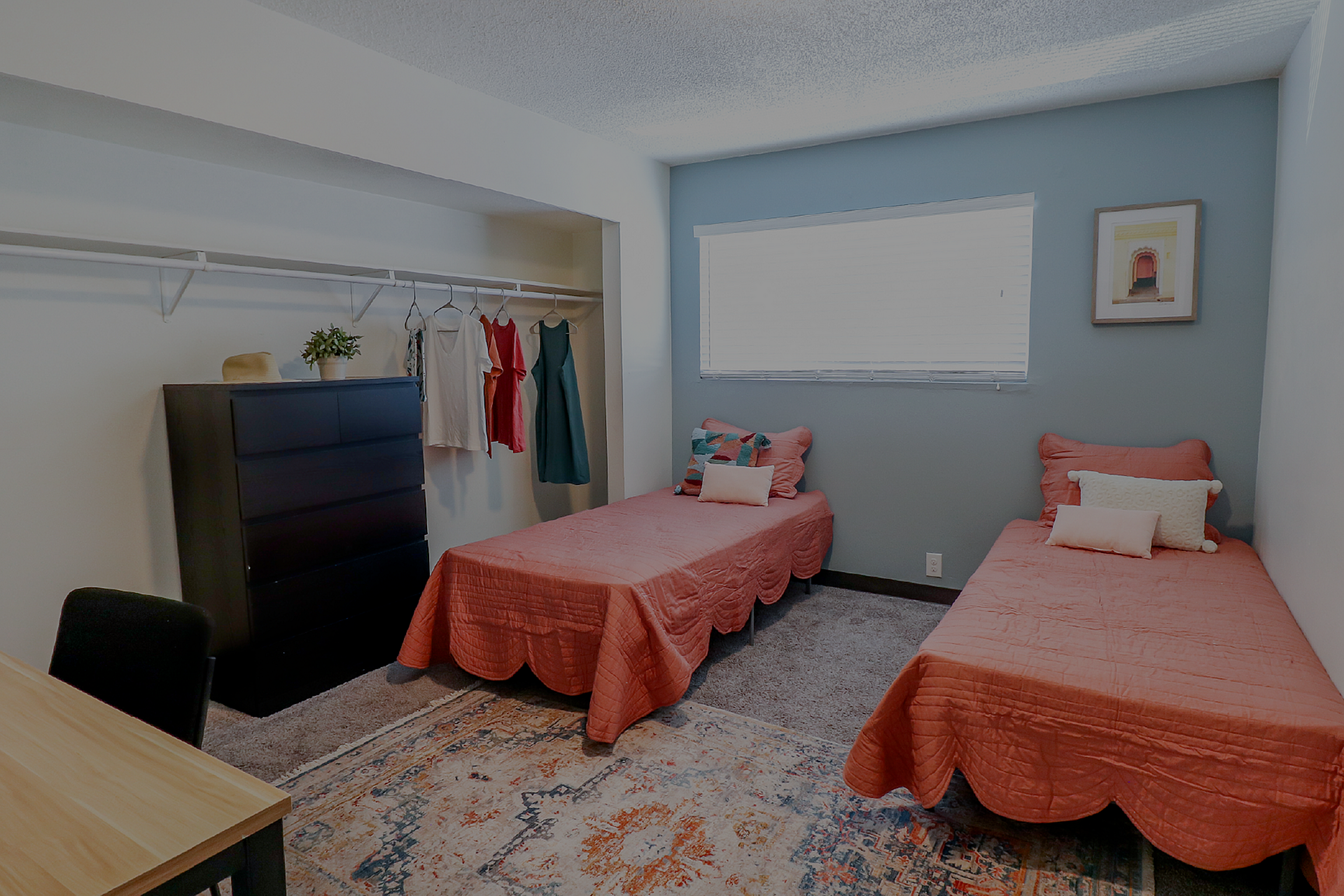 Chic bedroom with twin beds, vibrant coral bedding, open closet space, elegant dresser, and relaxing ambiance.