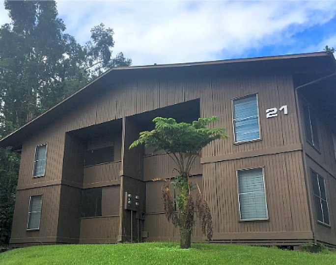Charming two-story wooden apartment building surrounded by lush greenery and clear blue skies, promising a serene living environment.