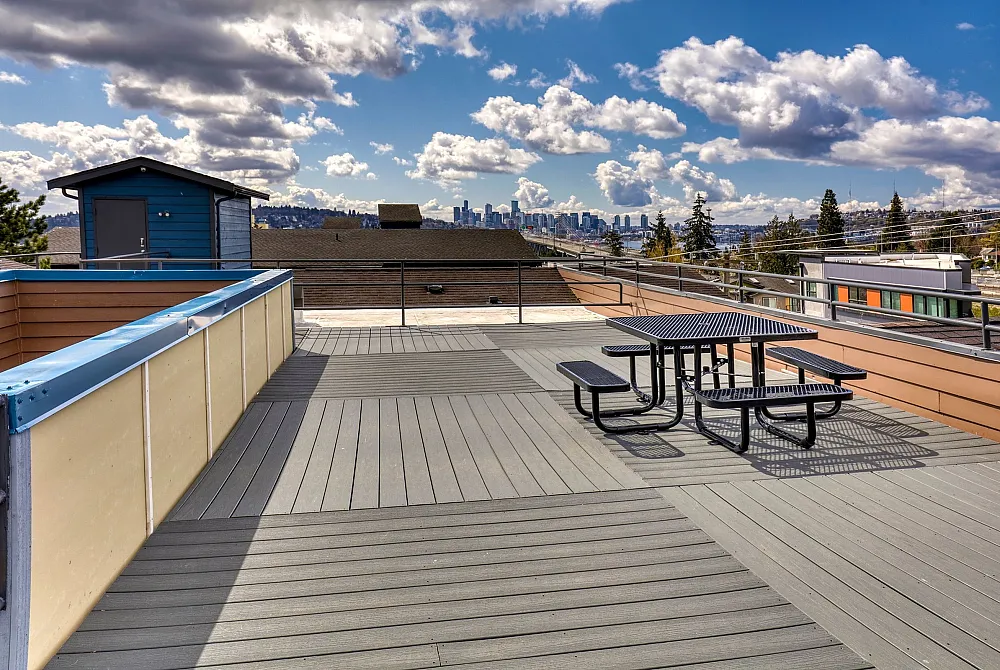 Expansive rooftop terrace with stunning cityscape views and ample seating under a vibrant blue sky with scattered clouds.