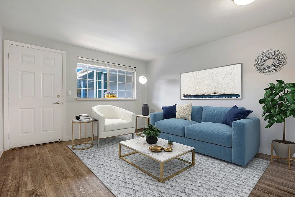 Bright and inviting living room with elegant hardwood flooring, a plush blue sofa, and a chic white armchair. Accentuated by contemporary decor and natural light from a large window.