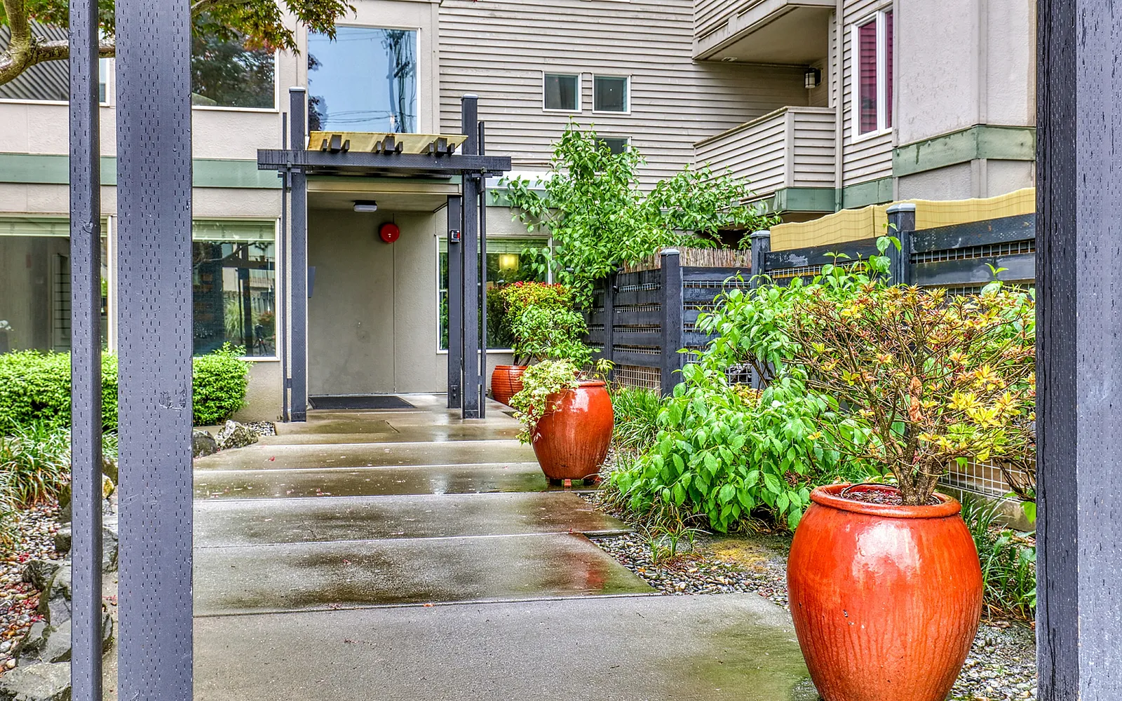 Charming apartment entrance with modern architectural design, lush greenery, and elegant red planters, offering a welcoming ambiance.