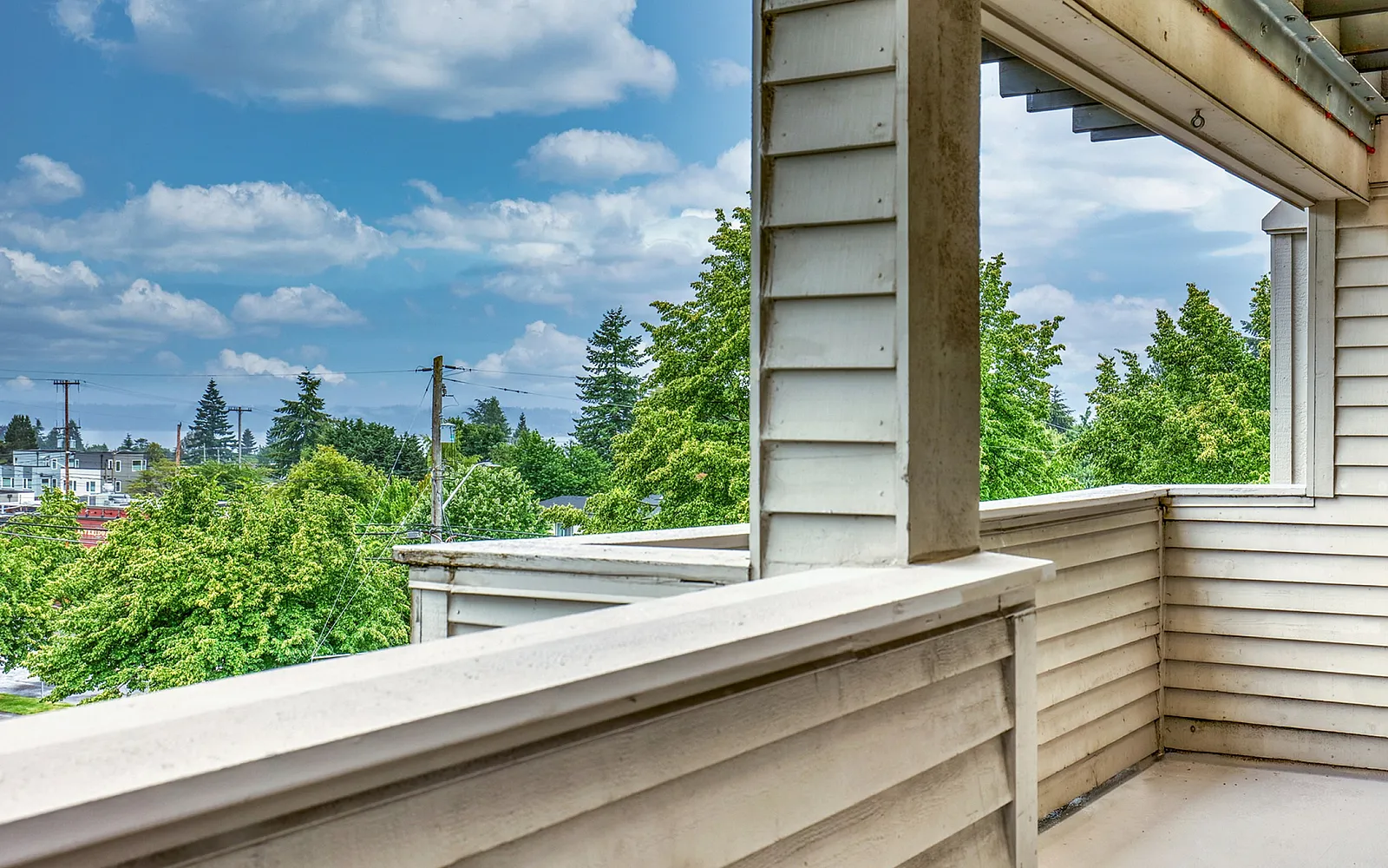 Charming apartment balcony with a serene view of lush green trees and blue sky, offering a perfect escape for relaxation.