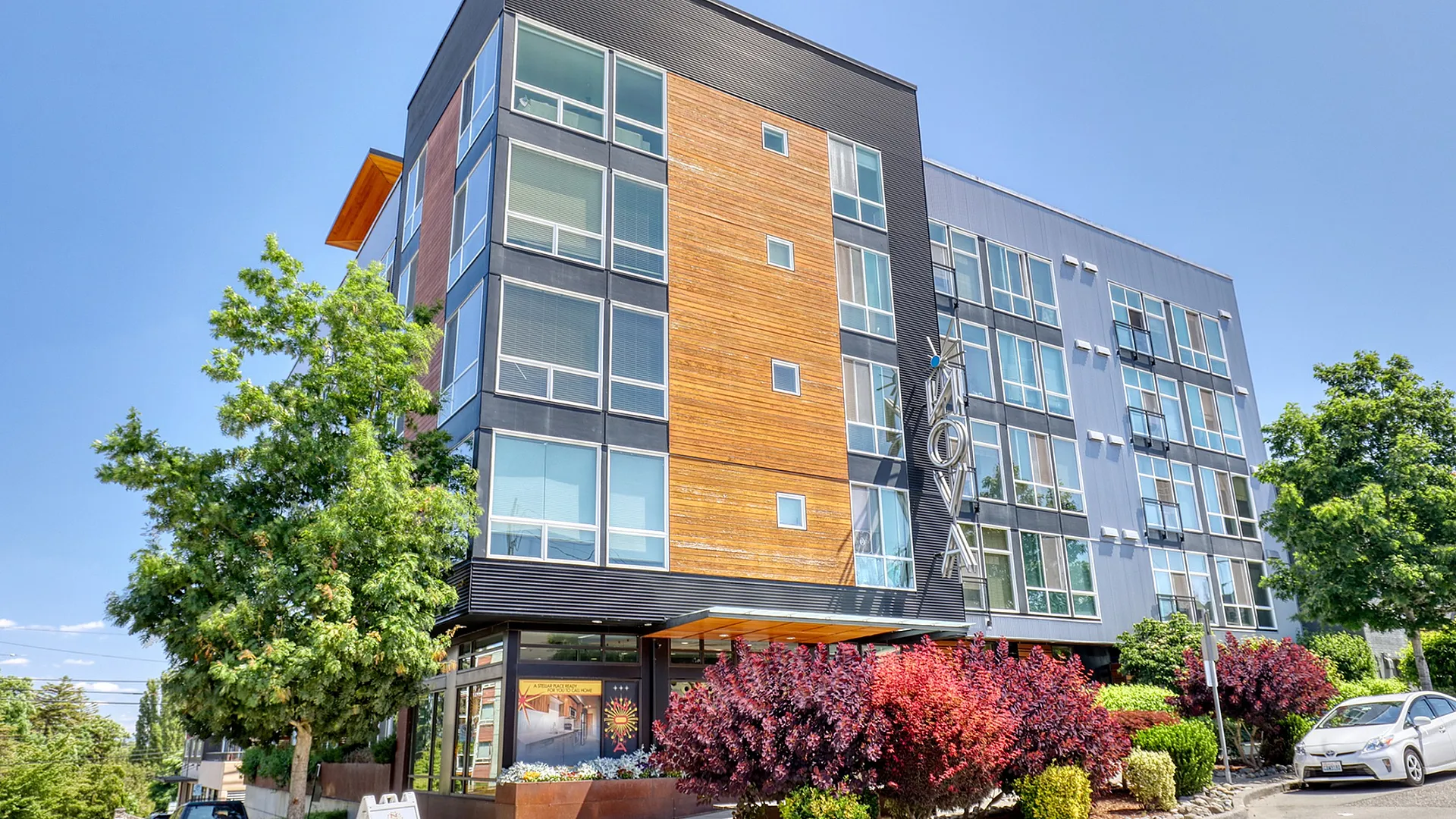 Contemporary apartment building with modern design, large windows, and vibrant landscaping under a clear blue sky.