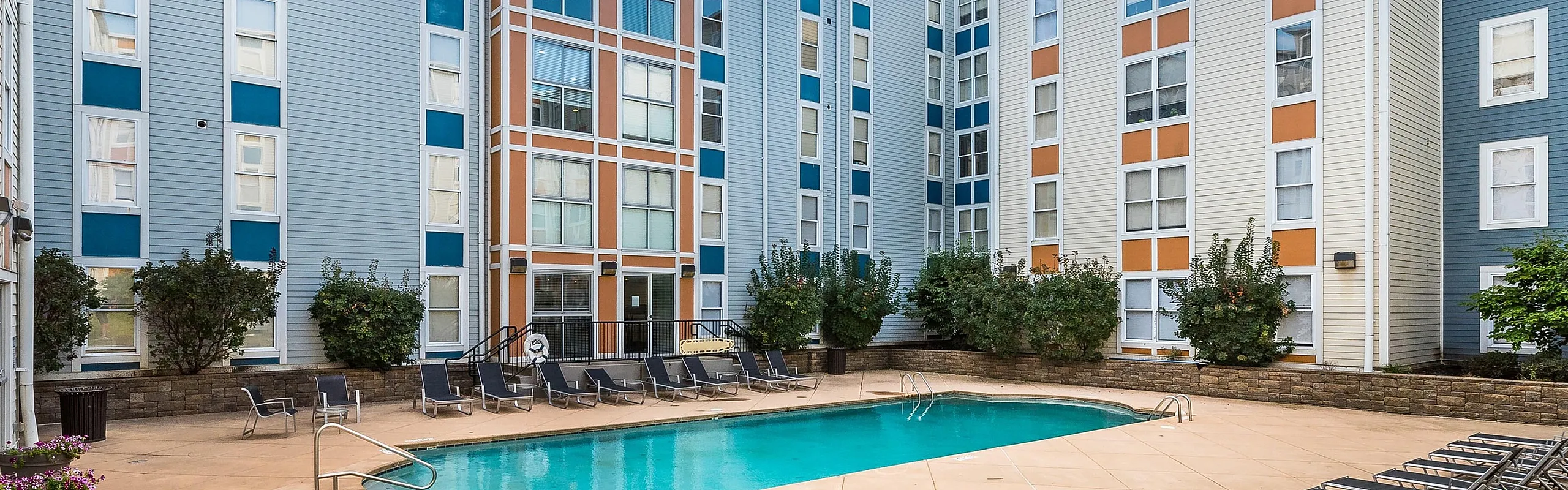 Modern apartment complex with vibrant facade overlooking a pristine swimming pool surrounded by stylish lounge chairs.