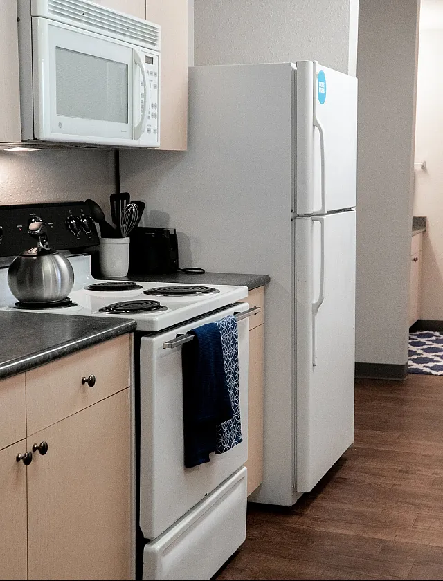 Modern kitchen with sleek appliances, white cabinetry, and warm hardwood floors leading to a cozy bedroom.