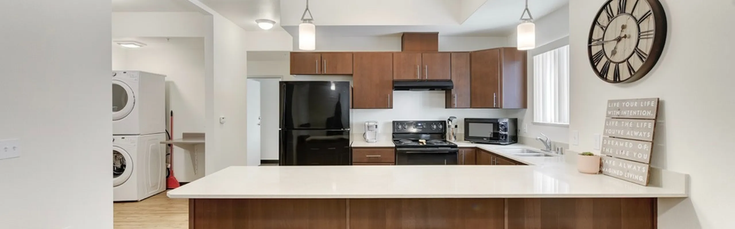 Modern kitchen with sleek countertops, dark wood cabinetry, and stylish barstools under pendant lighting. Equipped with state-of-the-art appliances and in-unit laundry.