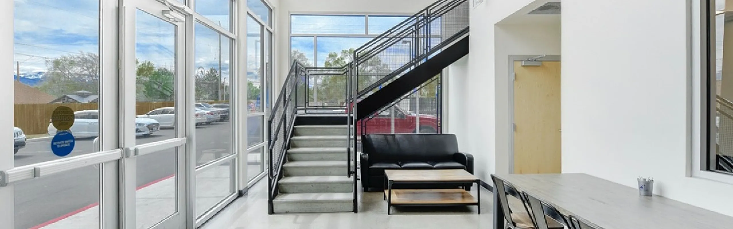 Bright, modern lobby with large windows, stylish staircase, and cozy seating area, perfect for welcoming guests.