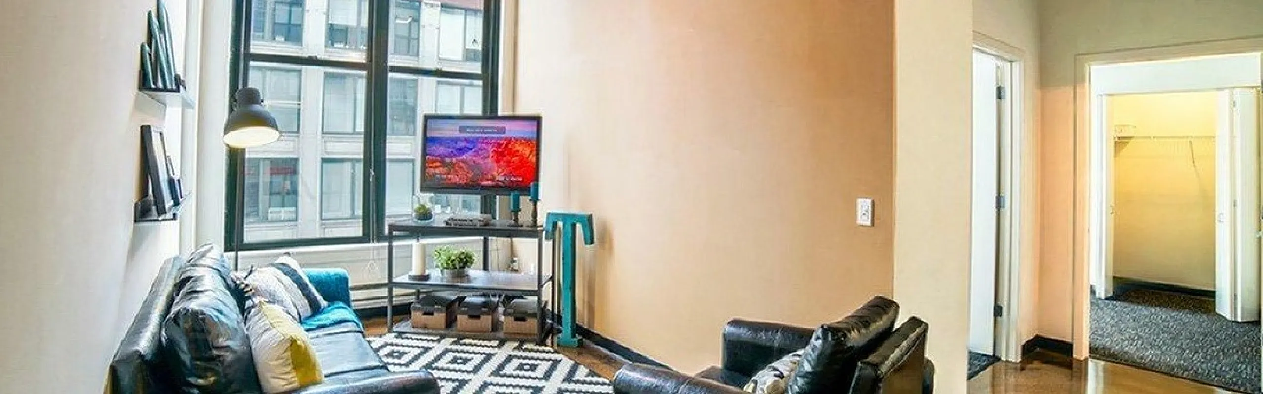Chic urban living room with industrial charm, featuring exposed beams, large windows, leather sofas, and stylish geometric rug.