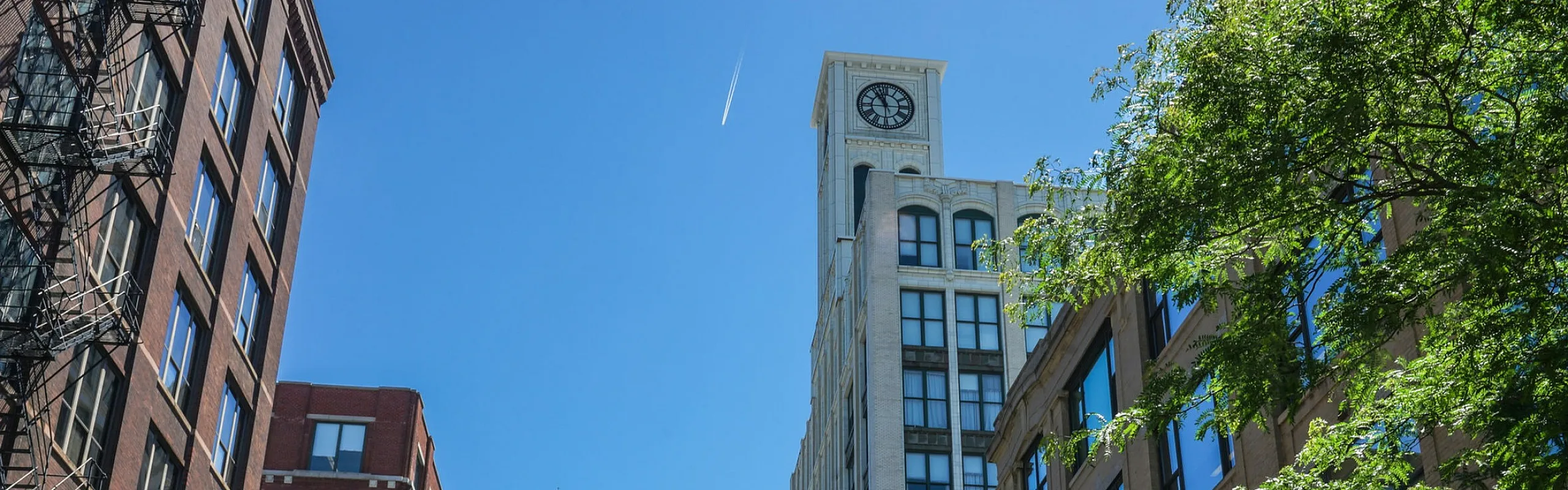 Dynamic urban streetscape featuring classic architecture and a prominent clock tower under a clear blue sky.