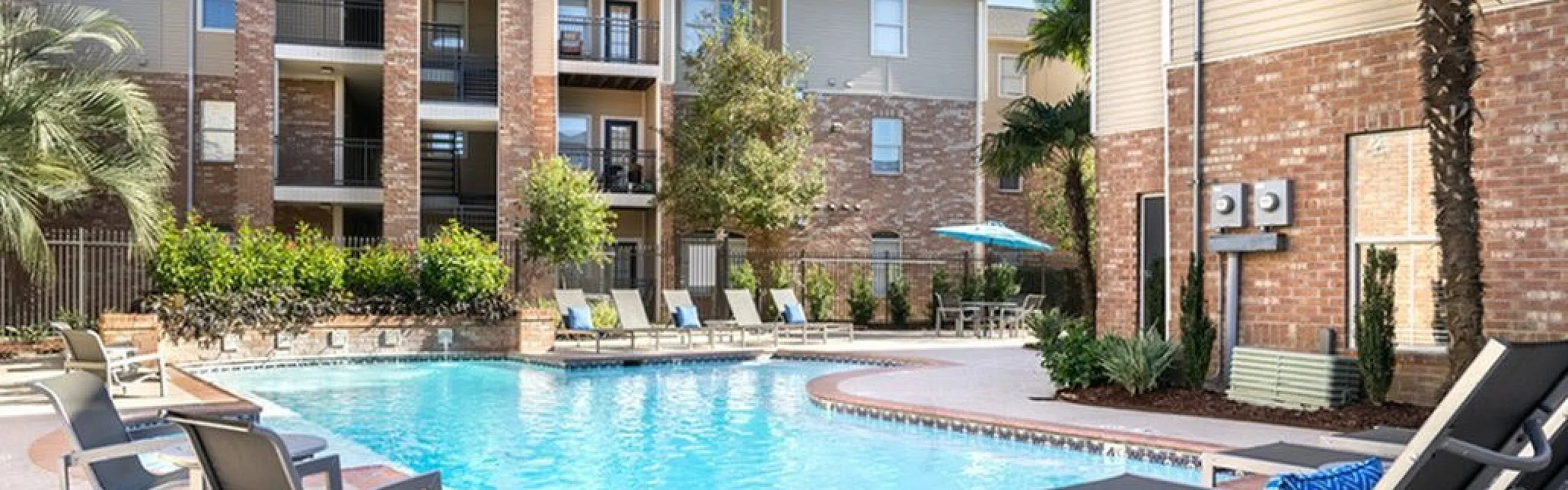 Inviting apartment complex with a sunlit pool area, surrounded by lush greenery and comfortable lounge chairs, showcasing modern architecture.