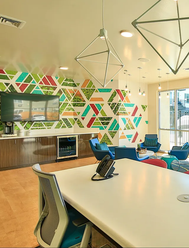 Bright and modern communal lounge area featuring vibrant geometric wall art, sleek furnishings, and large windows with a poolside view.