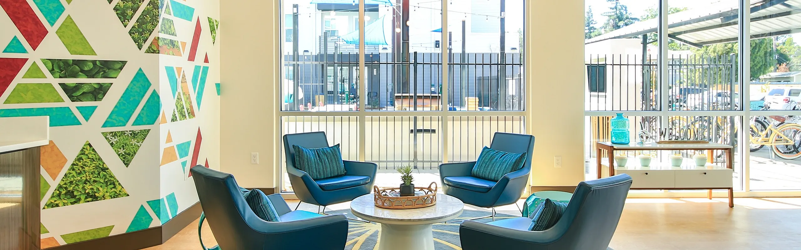 Bright and inviting lounge area with colorful geometric wall art, stylish blue chairs, and large windows offering natural light.